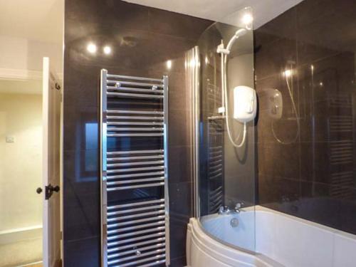 a bathroom with a tub and a shower with a mirror at Cinderbarrow Cottage in Levens