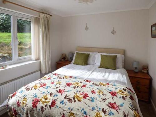 a bedroom with a bed with a floral comforter and a window at Simdda Wen Cottage in Llanddona