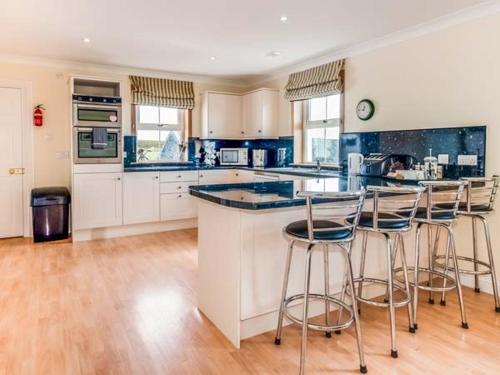 a kitchen with white cabinets and bar stools at Little Laight in Cairnryan