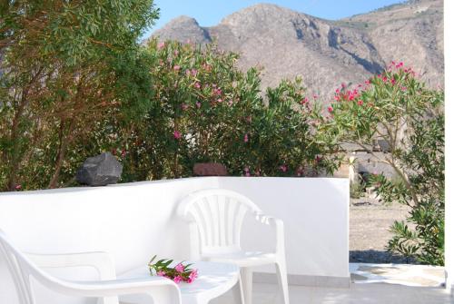 two white chairs and pink flowers on a white wall at Apollo Rooms in Perissa