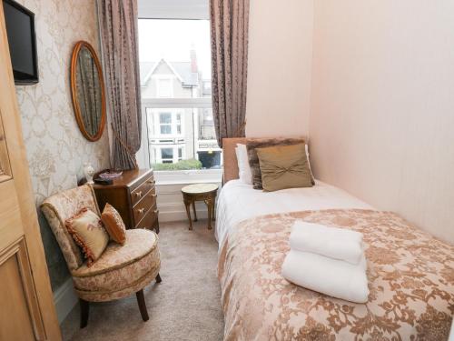 Un dormitorio con una cama y una silla y una ventana. en Abbeylands House, en Llandudno
