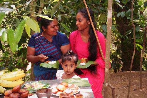 twee vrouwen en een kind staan naast een tafel met eten bij Retiyagama Eco Resort in Teldeniya