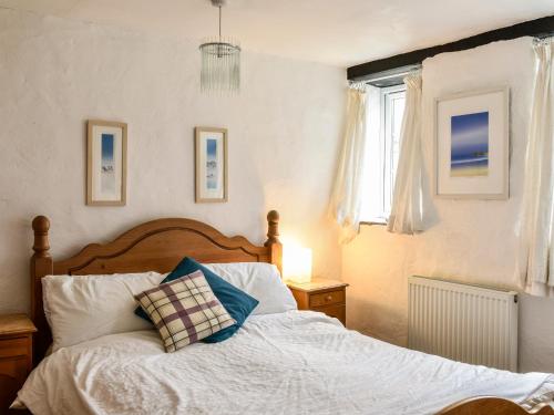 a bedroom with a bed with a wooden headboard and a window at Threshings Cottage in Tintagel