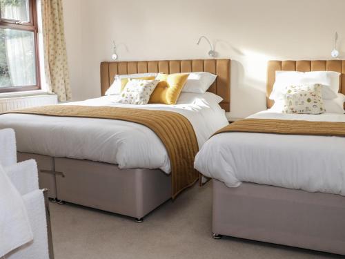 a bedroom with two beds with white sheets and gold pillows at Wrens Nest in Coreley
