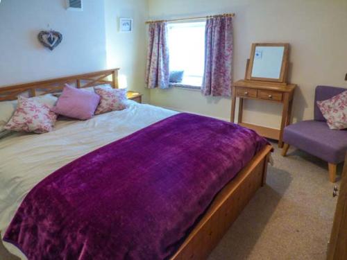 ein Schlafzimmer mit einem großen Bett mit einer lila Decke in der Unterkunft Bobbin Cottage in Matlock