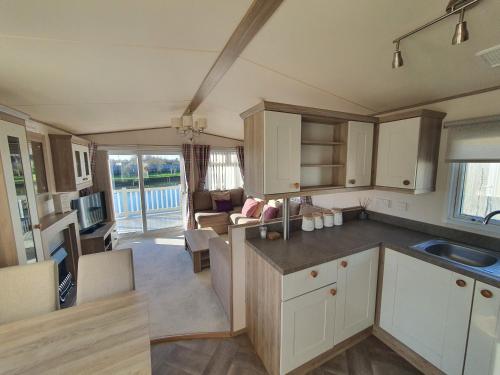 a kitchen with white cabinets and a living room at Cosy caravans Meadow lake Golden Palm Resort in Chapel Saint Leonards