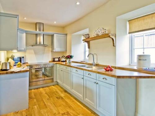 a large kitchen with white cabinets and wooden floors at The Old Farmhouse in Bowsden