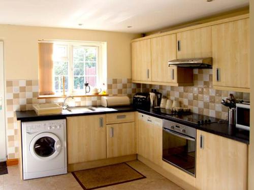 a kitchen with wooden cabinets and a washer and dryer at Farmhouse Cottage in Pentraeth