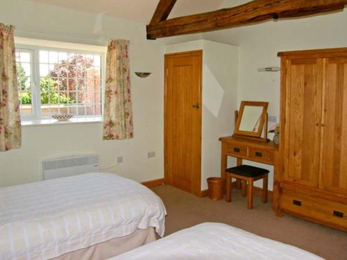 a bedroom with two beds and a dresser and a mirror at Byre Cottage in Nesscliffe