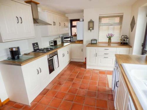 a kitchen with white cabinets and an orange tile floor at Beacon Cottage in Great Malvern