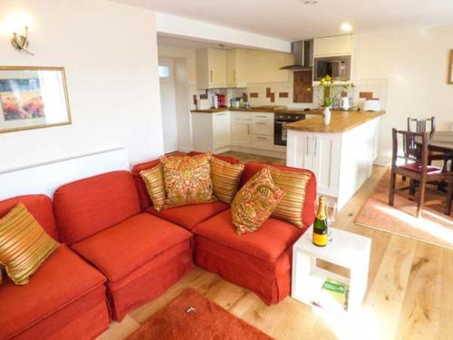 een woonkamer met een rode bank en een keuken bij Kestrel Cottage in Grange Over Sands