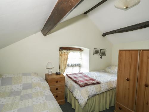 a bedroom with two beds and a dresser and a window at Gardeners Cottage in Hesket Newmarket