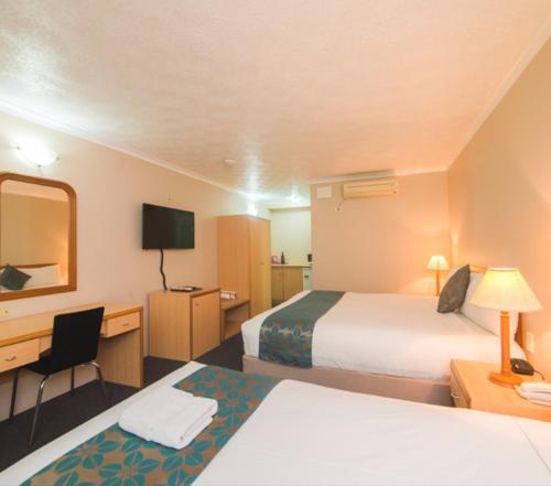 a hotel room with two beds and a desk at Harbour Sails Motor Inn in Gladstone