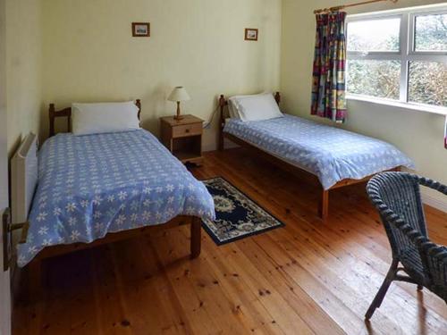 a bedroom with two beds and a chair and a window at Number 12 in Mulranny