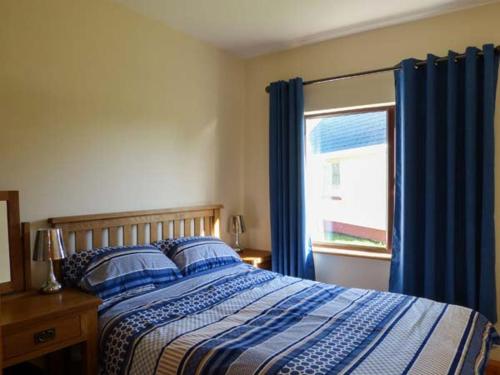 a bedroom with a bed with blue curtains and a window at The Well House in Kinvara