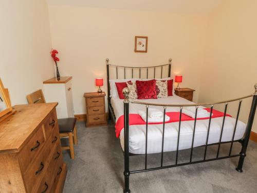 Cette chambre comprend un lit avec des oreillers rouges et une commode. dans l'établissement Kitchen Cottage, à Sutton
