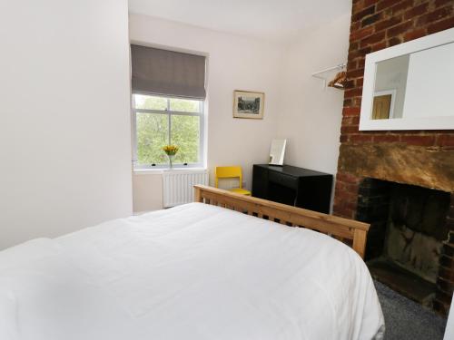 1 dormitorio con cama blanca y chimenea en The Flat, en Keighley