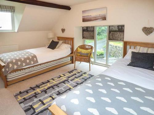 a bedroom with two beds and a chair and a window at Honeypot Cottage in Kendal