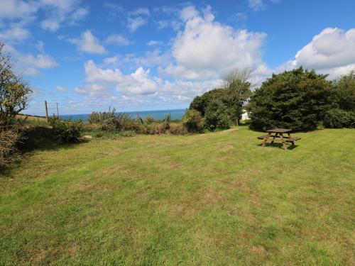 a picnic table in a field with the ocean in the background at The Granary Cottage in Llangranog