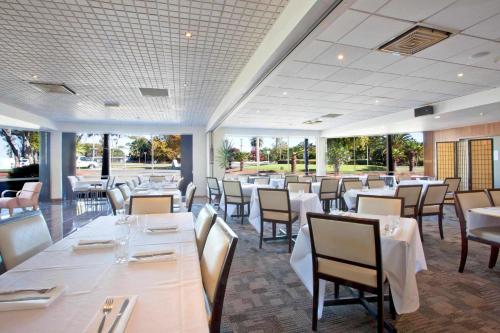 a restaurant with white tables and chairs and windows at Auckland Airport Kiwi Hotel in Auckland