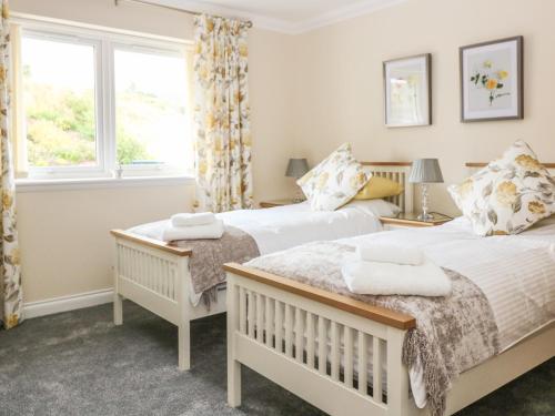 two beds in a room with two windows at Burnside Cottage in Portree