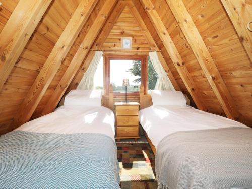 two beds in a wooden attic room with a window at Apple Tree Lodge in Gillingham