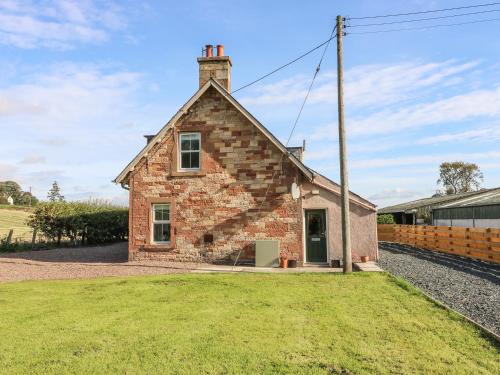an old brick house with a grass yard in front of it at Bonjedward Mill Farm Cottage in Jedburgh