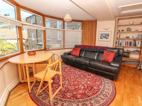 a living room with a black leather couch and a table at Surf Song in Penzance