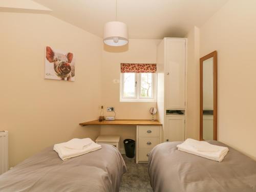 two beds in a room with a desk and a window at The Old Sty in Whiston