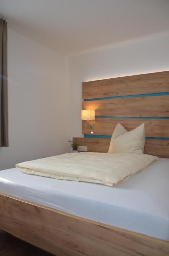 Bett mit einem Kopfteil aus Holz und weißer Bettwäsche in der Unterkunft Platzwirt in Unterschneidheim