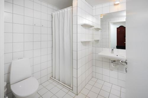 a white tiled bathroom with a toilet and a sink at Tornøes Hotel in Kerteminde