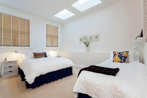 two beds in a bedroom with white walls and windows at Veeve - Charming Hampstead Apartment in London