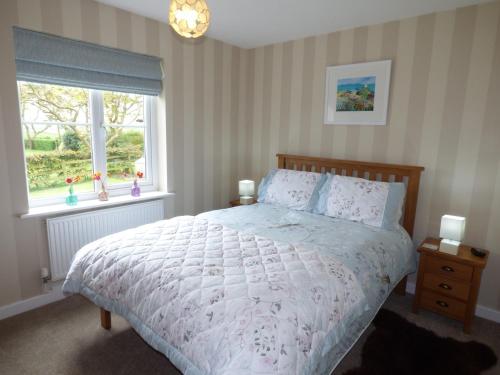 a bedroom with a bed with a white comforter and a window at Hafod Cottage in Cemaes Bay