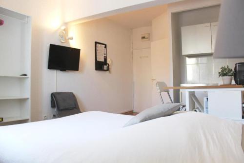 a bedroom with a white bed and a desk and a tv at Studios Raphael in Saint-Raphaël