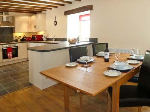 una cocina con una mesa de madera con platos y botellas de vino en Beudy Bach en Abergele