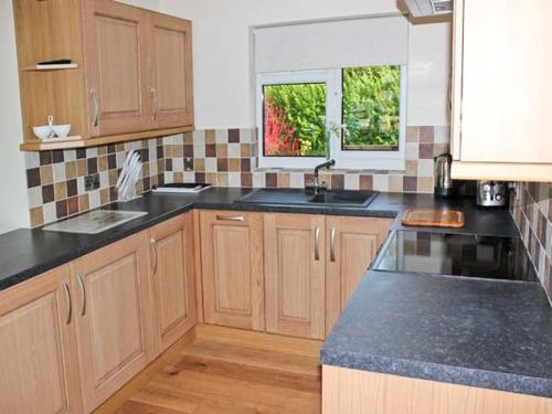 a kitchen with wooden cabinets and black counter tops at Moat Farm Cottage in Wood Dalling