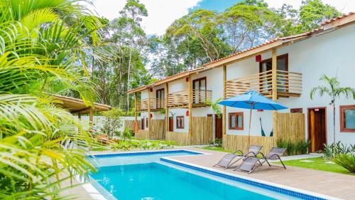 a house with a swimming pool and two chairs and an umbrella at Pousada Vila Mangaba in Arraial d'Ajuda