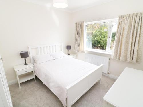 ein weißes Schlafzimmer mit einem weißen Bett und einem Fenster in der Unterkunft Wysteria Cottage in Windermere