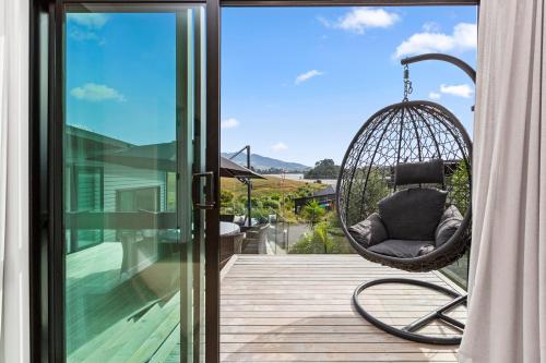 a hanging chair on a porch with a view at R and R at Robertson - Raglan Holiday Home in Raglan