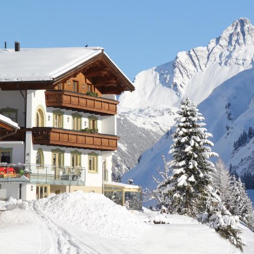 a building in the snow with a snow covered mountain at Pension Bergland in Lech am Arlberg