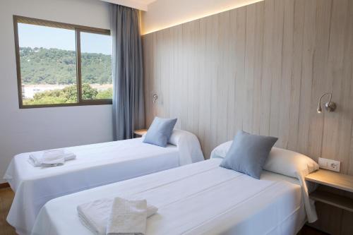 two beds in a hotel room with a window at GHT Aparthotel Tossa Park in Tossa de Mar