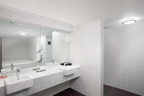 a bathroom with two sinks and a mirror and a tub at Rydges Canberra in Canberra
