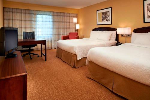 a hotel room with two beds and a desk and a television at Sonesta Select Detroit Novi in Novi