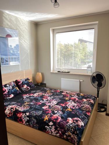 a bedroom with a bed with a floral bedspread and a window at Apartament Jasna in Jastrzębia Góra