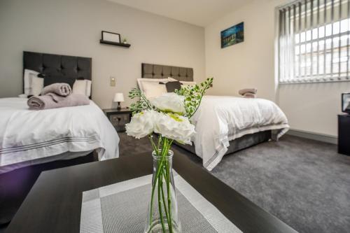 a bedroom with two beds and a vase with flowers on a table at Huddersfield Central Lodge in Huddersfield