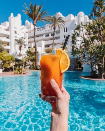 a person holding up a drink with an orange slice at Dreams Jardin Tropical Resort & Spa in Adeje