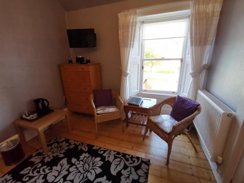 uma sala de estar com uma janela, 2 cadeiras e uma mesa em St Ronan's Hotel em Innerleithen