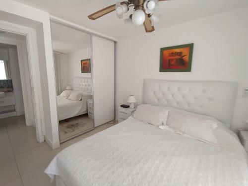 Dormitorio blanco con cama blanca y espejo en Apartamento Edificio Unique, Punta del Este, en Punta del Este