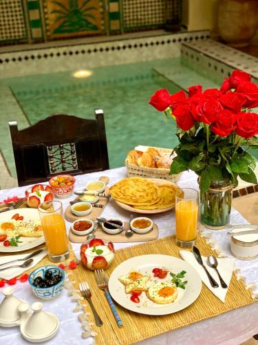 un tavolo con piatti di cibo e rose e una piscina di Riad Dar Talah a Marrakech