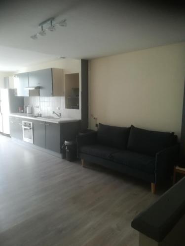 a living room with a black couch and a kitchen at Chambre simple avec WiFi châtellerault in Châtellerault
